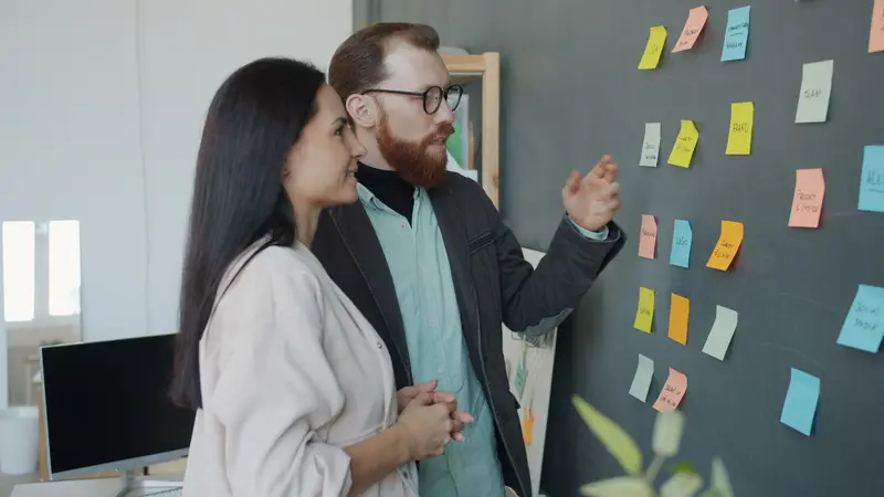 Two colleagues reviewing actions on an improvement board covered in notes