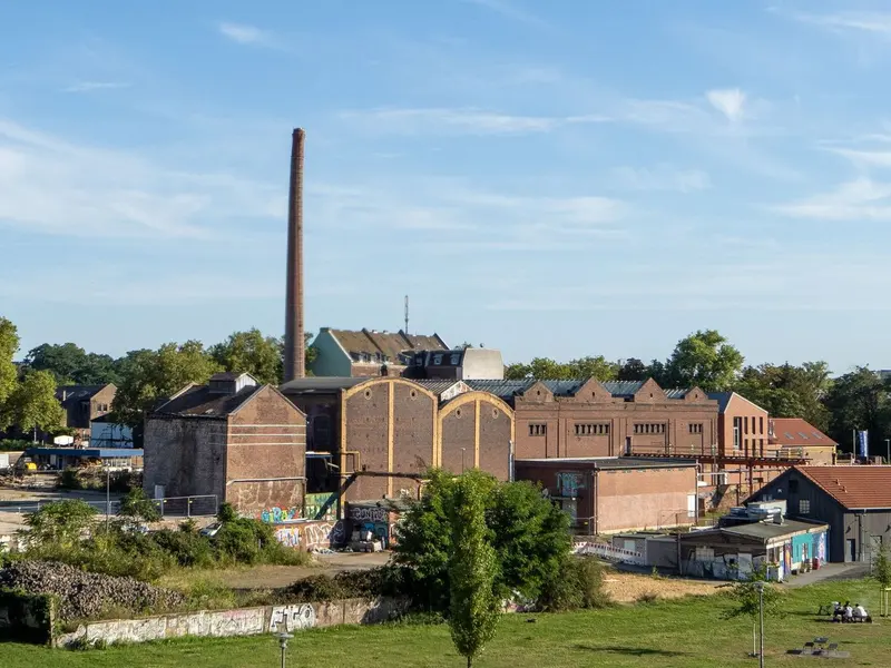 Brick factory buildings with pitched roofs and a tall chimney under a clear blue sky